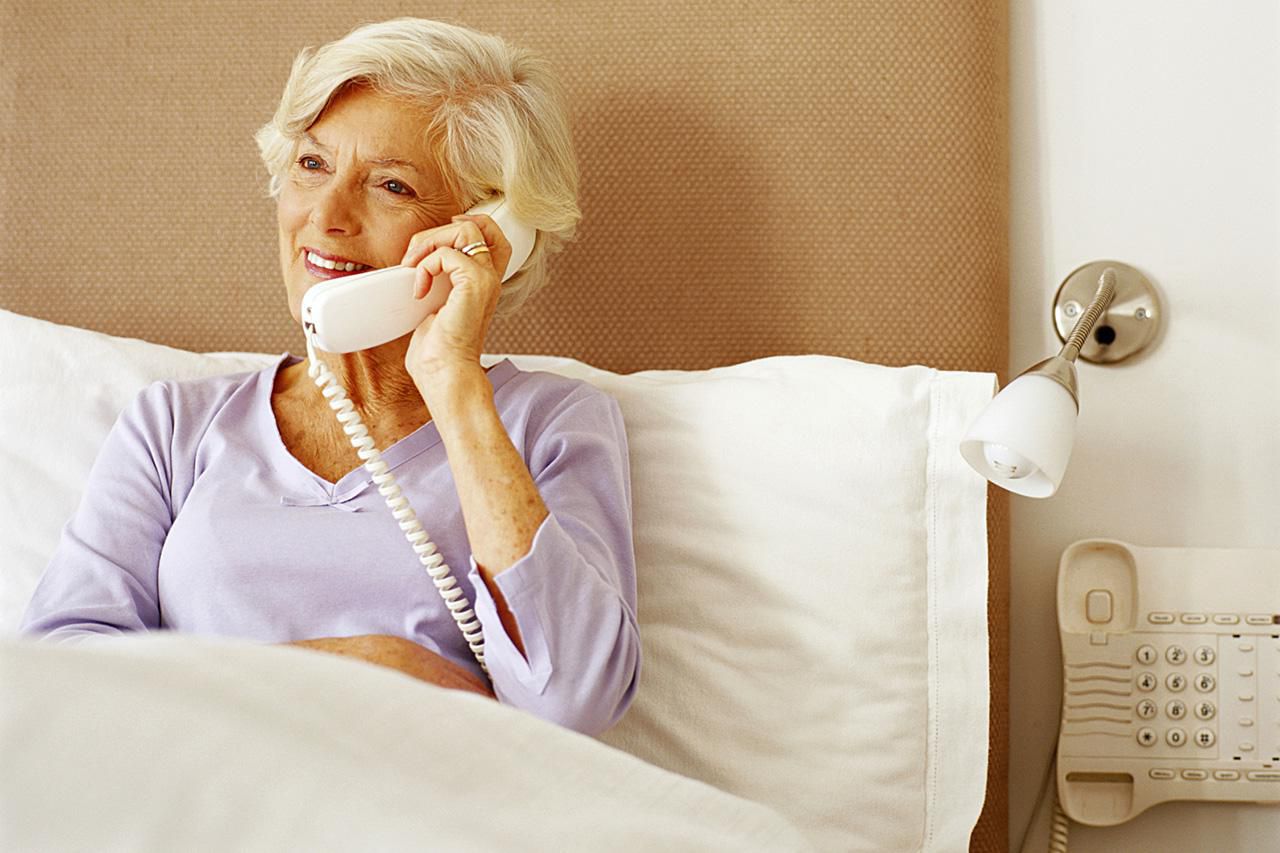 Ältere Frau im Bett sitzend, telefonierend