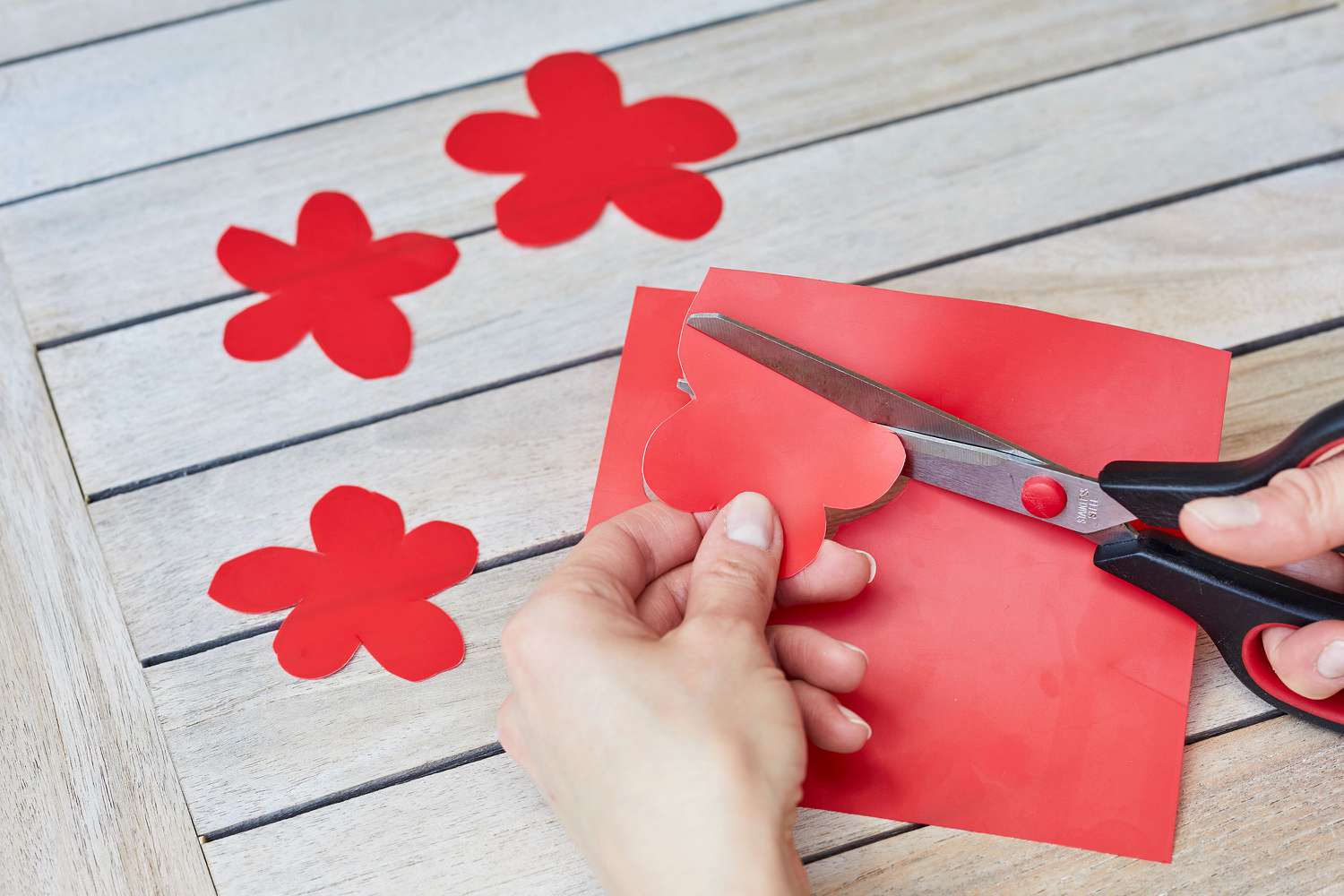 Formas de flores cortadas de uma pasta plástica vermelha com uma tesoura