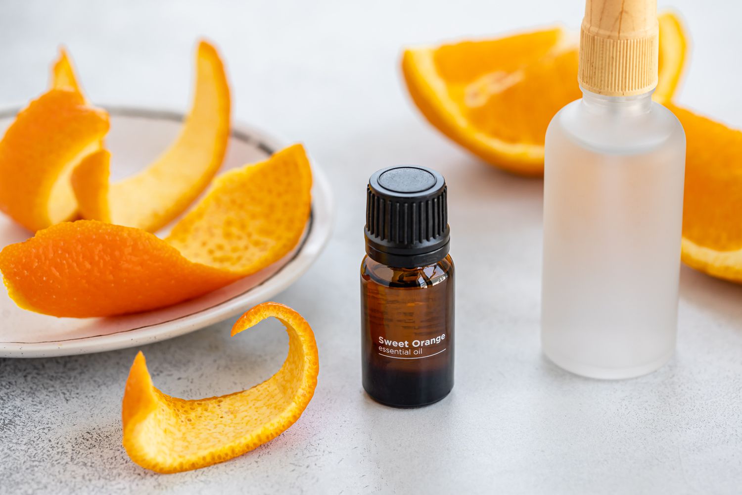 Ätherisches Orangenöl neben geschnittenen Orangenschalen und Sprühflasche