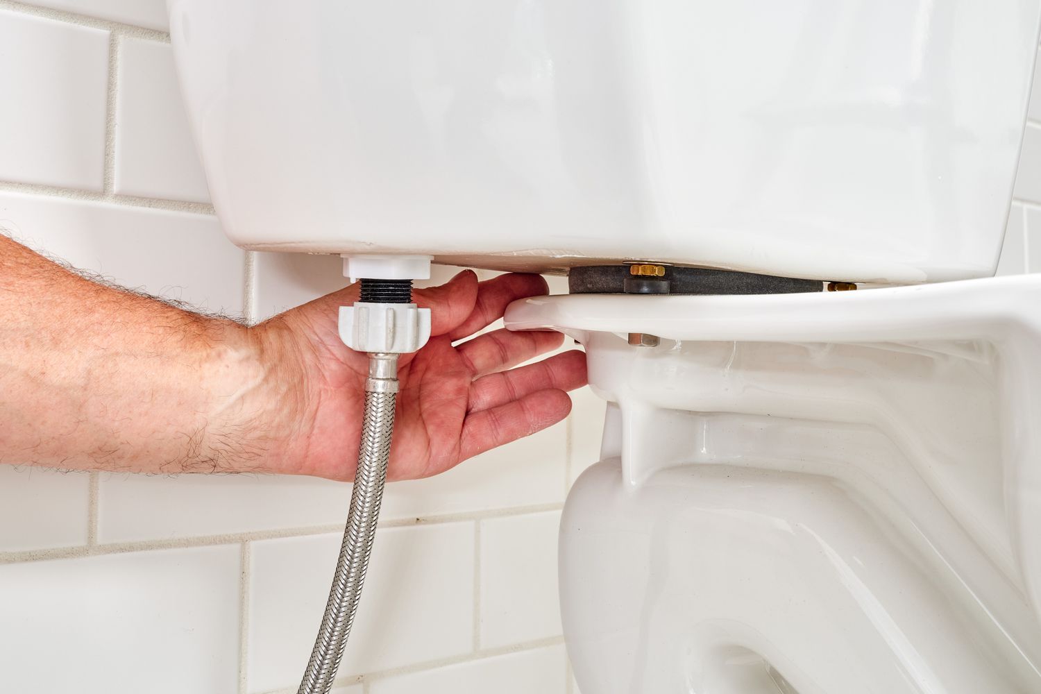 Handprüfung auf Undichtigkeiten hinter dem wieder installierten Wasserzulaufschlauch zum Toilettentank