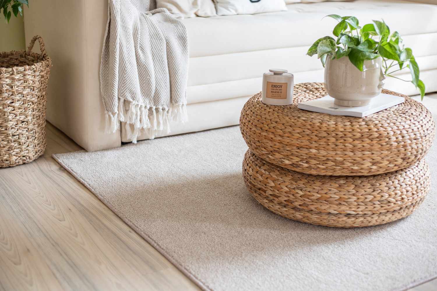 Weiße Couch und gestapelte Rattan-Poufs auf cremefarbenem Teppich