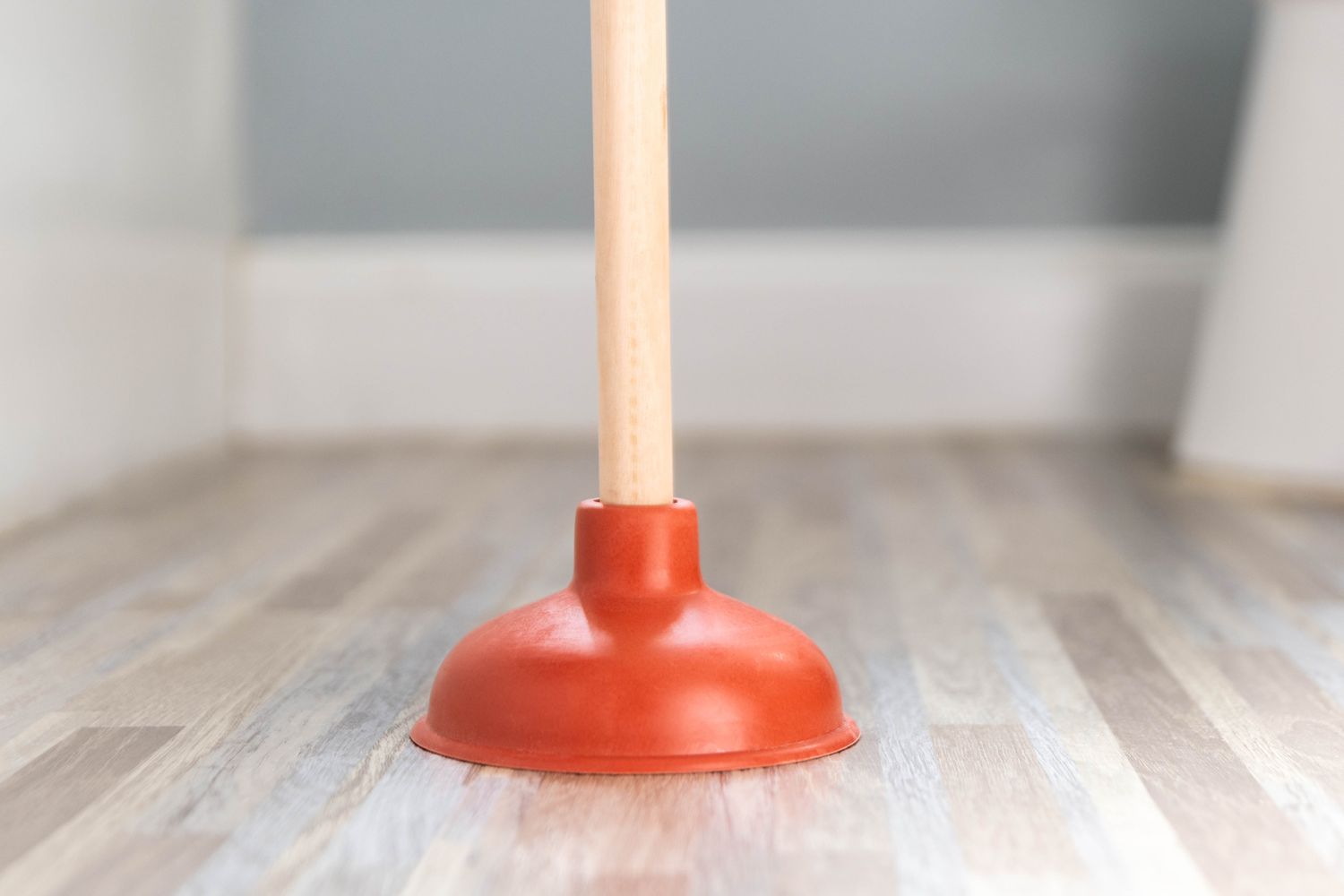 Clay-colored sink/standard plunger on bathroom floor