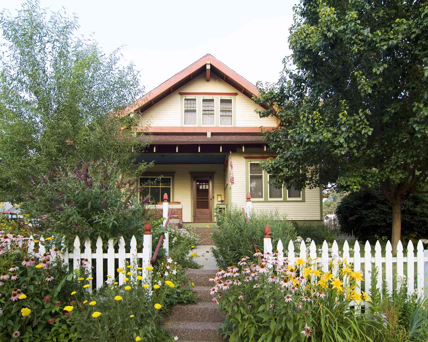 Bungalowhaus lachsfarben, außen beige und grün mit weißem Lattenzaun