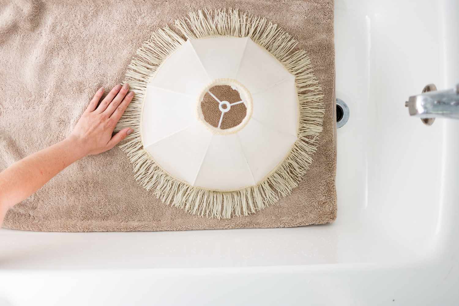 Abajur branco com franjas colocado sobre uma toalha marrom para secar na banheira