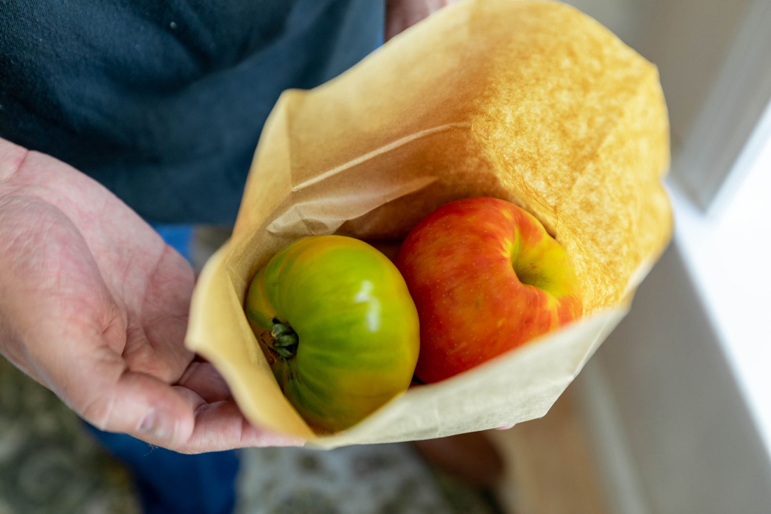 Tomate jaune-verte placée dans un sac en papier avec une pomme pour mûrir