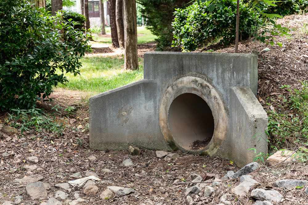 Large sewer main drain opening surrounded by wooded area and rocks