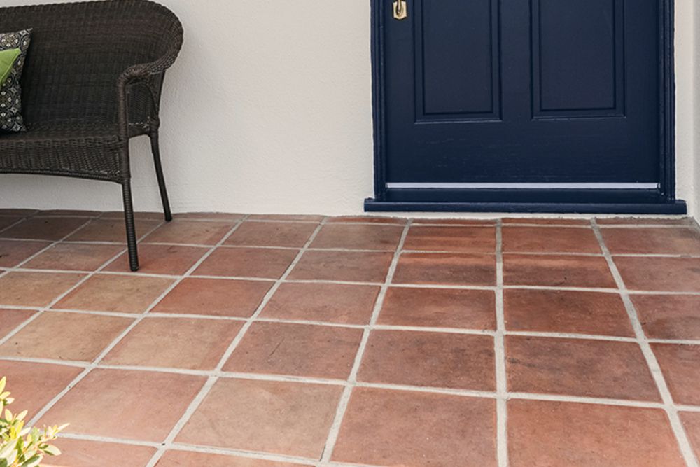 Terracotta floor tiles in front of blue front door entrance