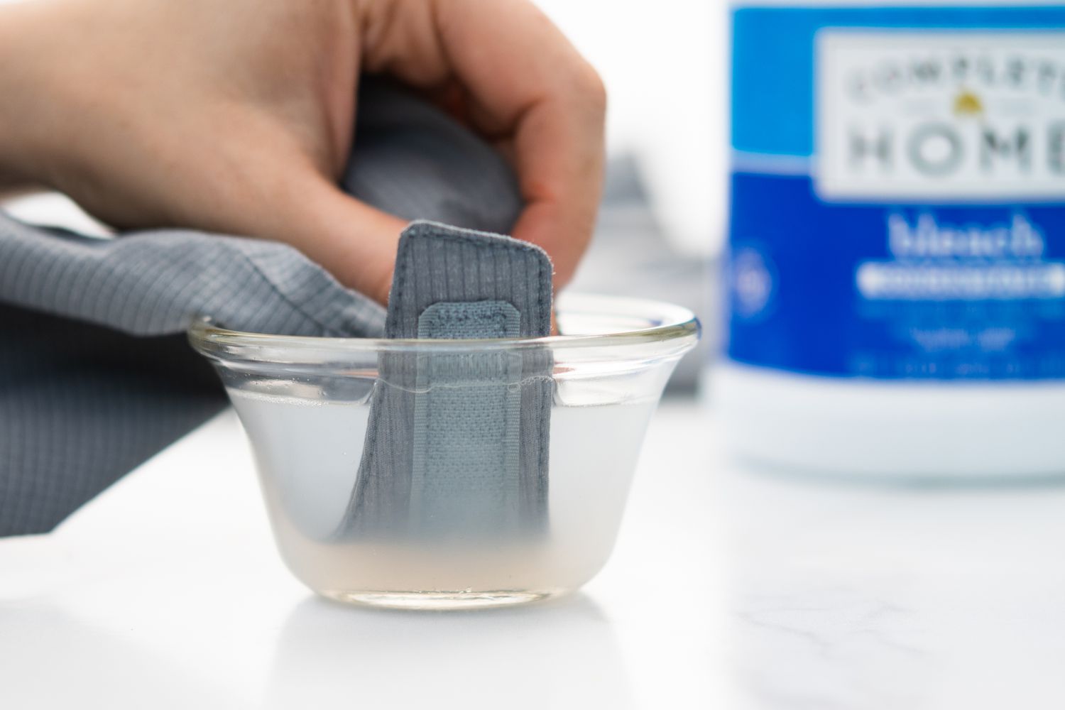 Klettverschluss von waschbarem Kleidungsstück in kleine Schüssel mit Wasser und sauerstoffbasiertem Bleichmittel getaucht