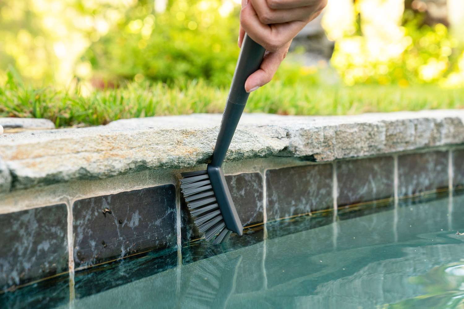 Escova de cerdas duras esfregando depósitos minerais no azulejo da piscina