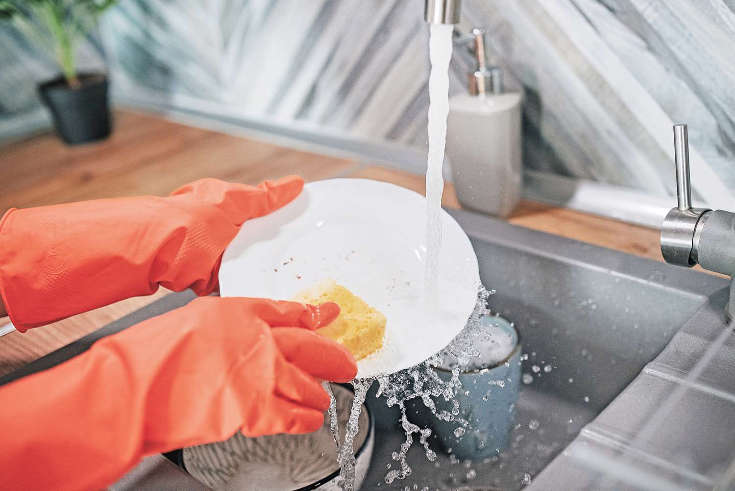 Schmutziges Geschirr wird mit orangefarbenen Handschuhen in der Spüle abgewaschen