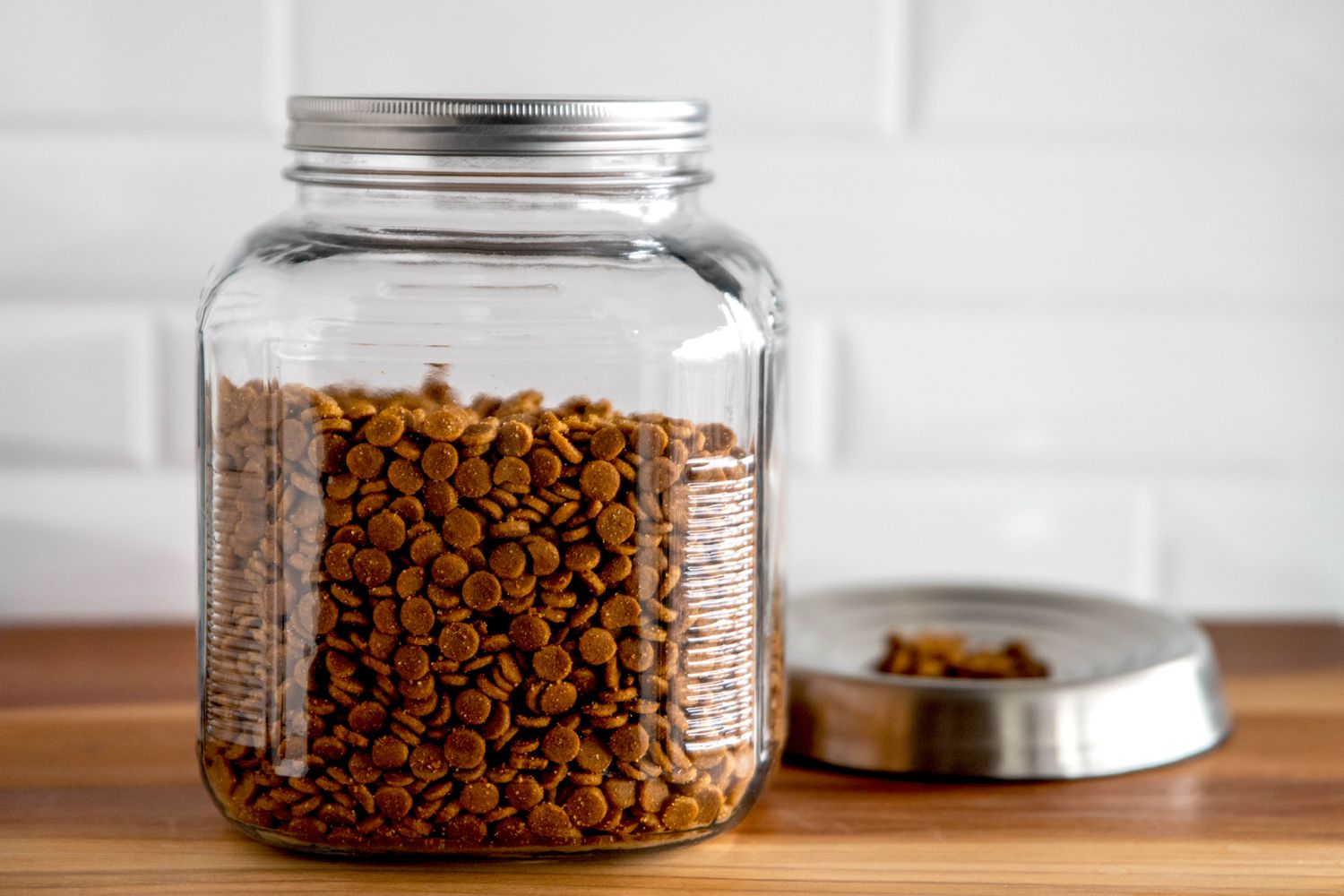 Pet food stored in closed glass container next to pan with some dog food pieces