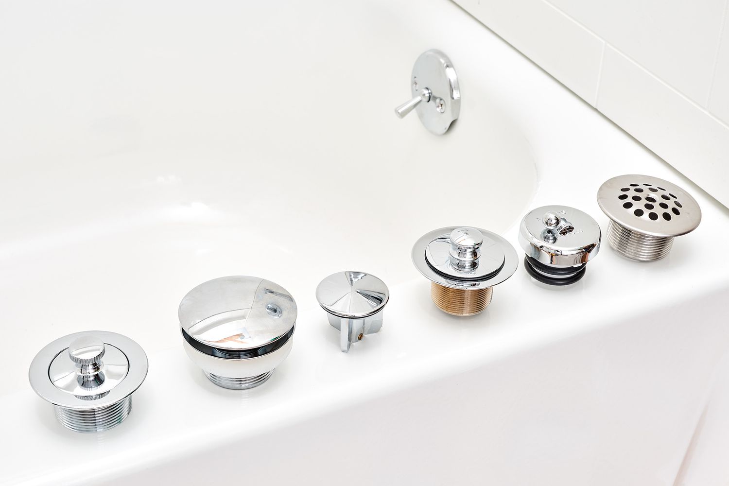 Six different types of drain stoppers lined on edge of tub