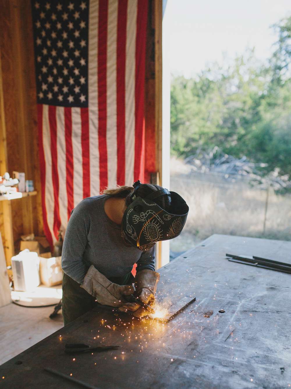 Kelly schweißt auf einem Tisch mit amerikanischer Flagge im Hintergrund.