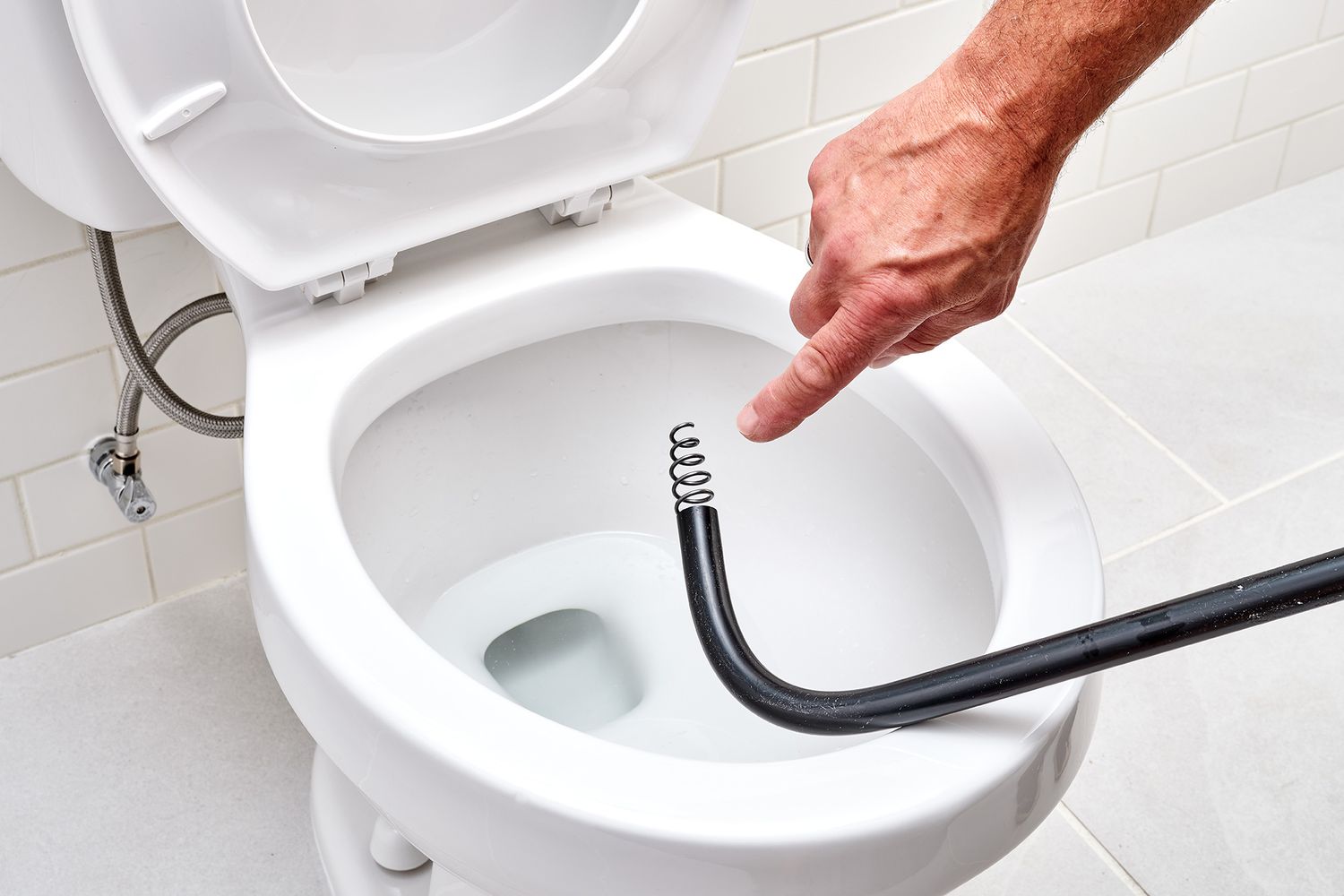 Toilet auger placed on toilet bowl with curled cable showing at end