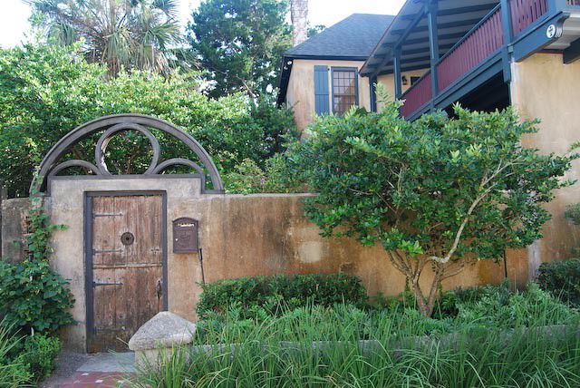 Casa antigua con muro de piedra y puerta de madera con portón de hierro y jardín de hierbas y enredaderas