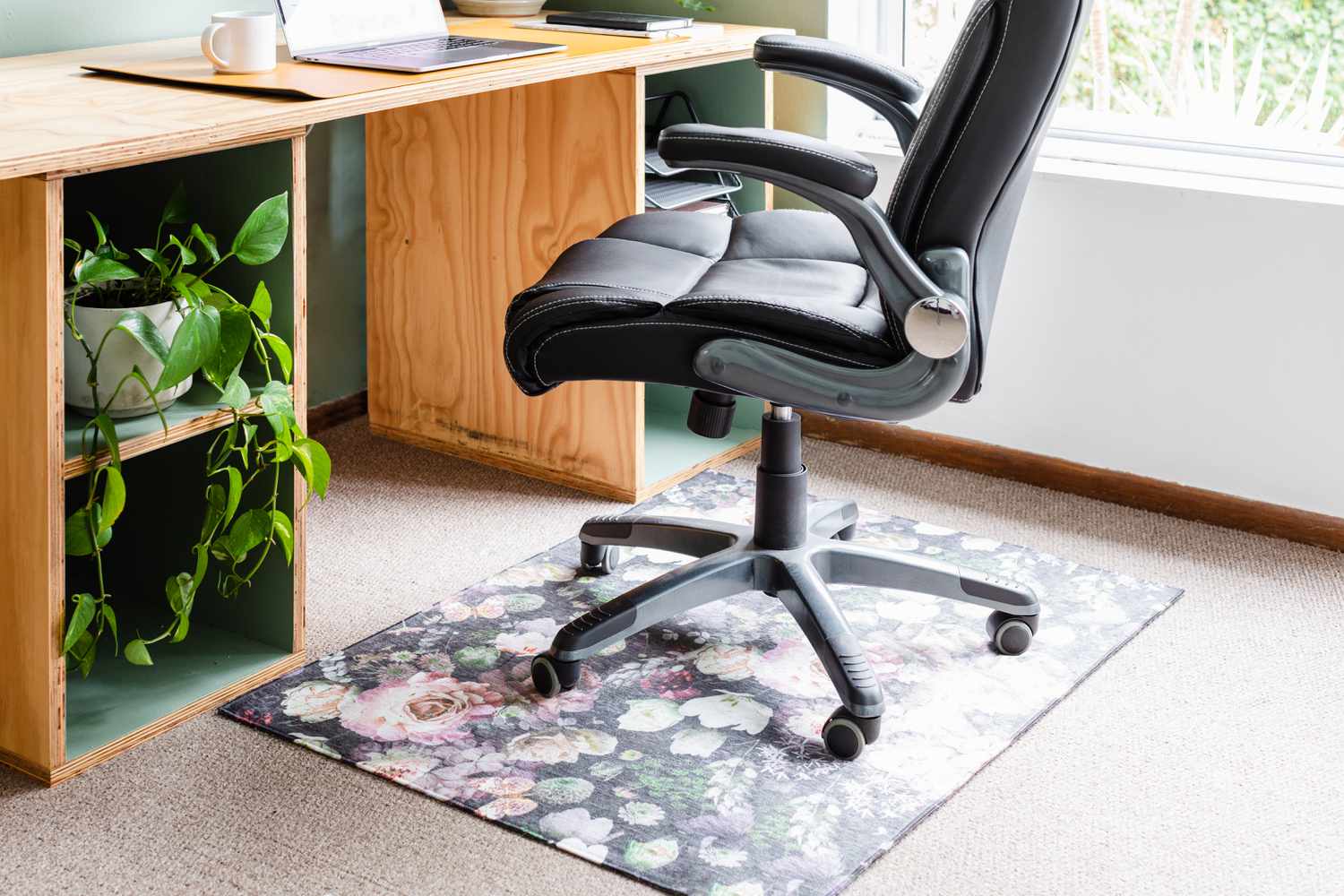 Bürostuhl auf geblümter und schwarzer Stuhlmatte neben Holzschreibtisch in Großaufnahme