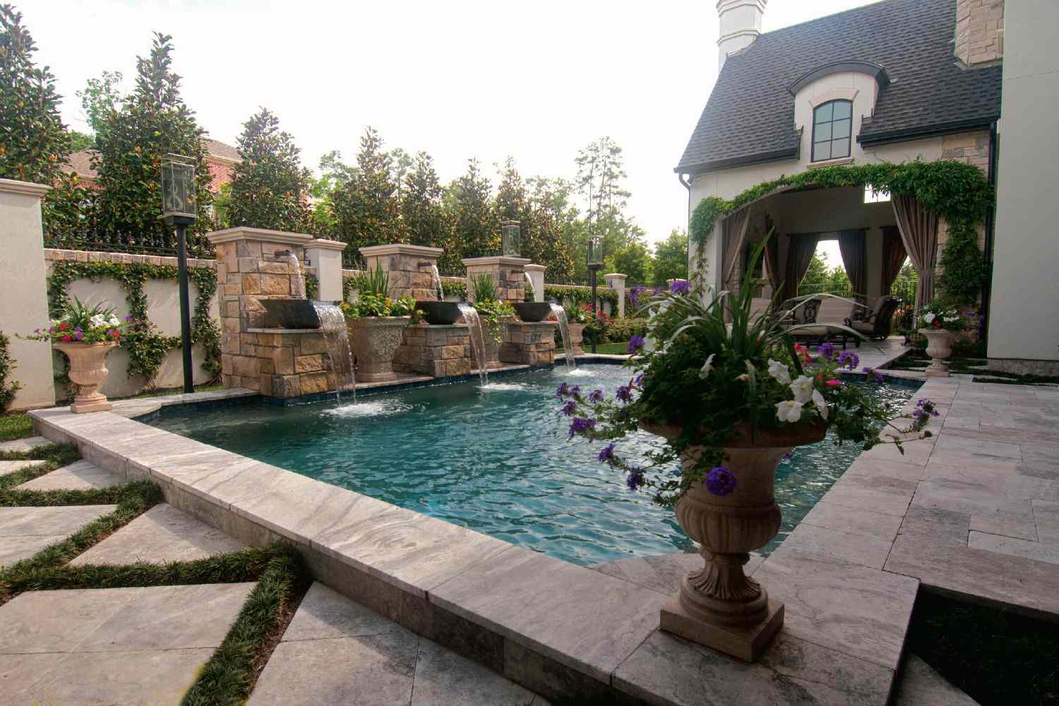 Rechteckiger mediterraner Pool mit Steinbrunnen und üppiger Bepflanzung.