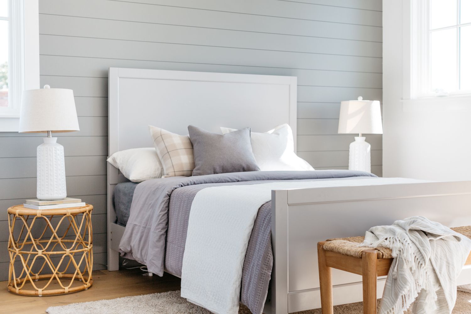 Chambre à coucher de style maison de ferme avec des accents de décoration gris clair et blanc à côté d'un banc boisé et des tables de nuit