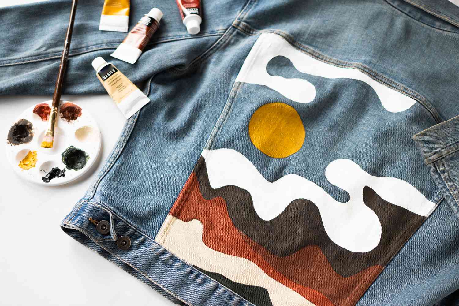 Parte de trás da jaqueta jeans com cena de paisagem pintada ao lado de materiais de pintura