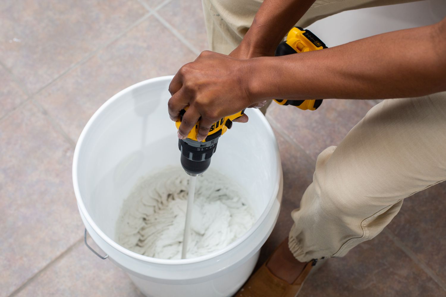 Unsanded grout mixed in white bucket with electric drill 