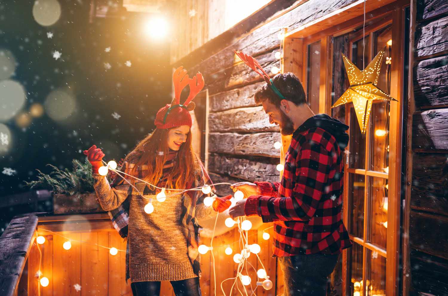 Pärchen im Urlaub auf einer Berghütte. Schmücken der Veranda mit Lichterketten für Weihnachten