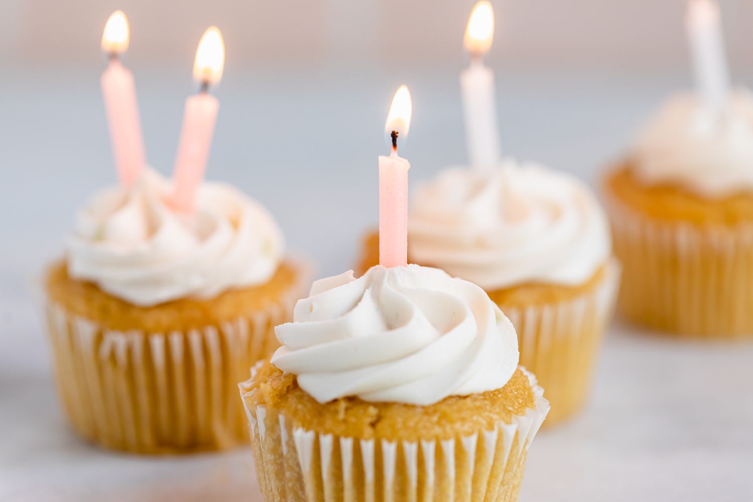 Velas de aniversário rosa-claro e brancas acesas em cupcakes foscos
