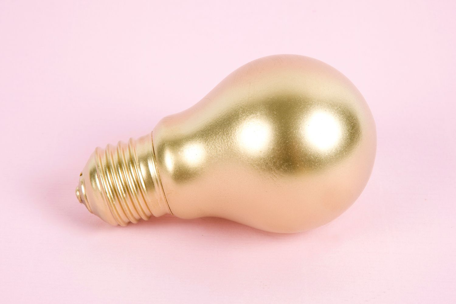 Goldfarbene Glühbirne auf einer rosafarbenen Oberfläche