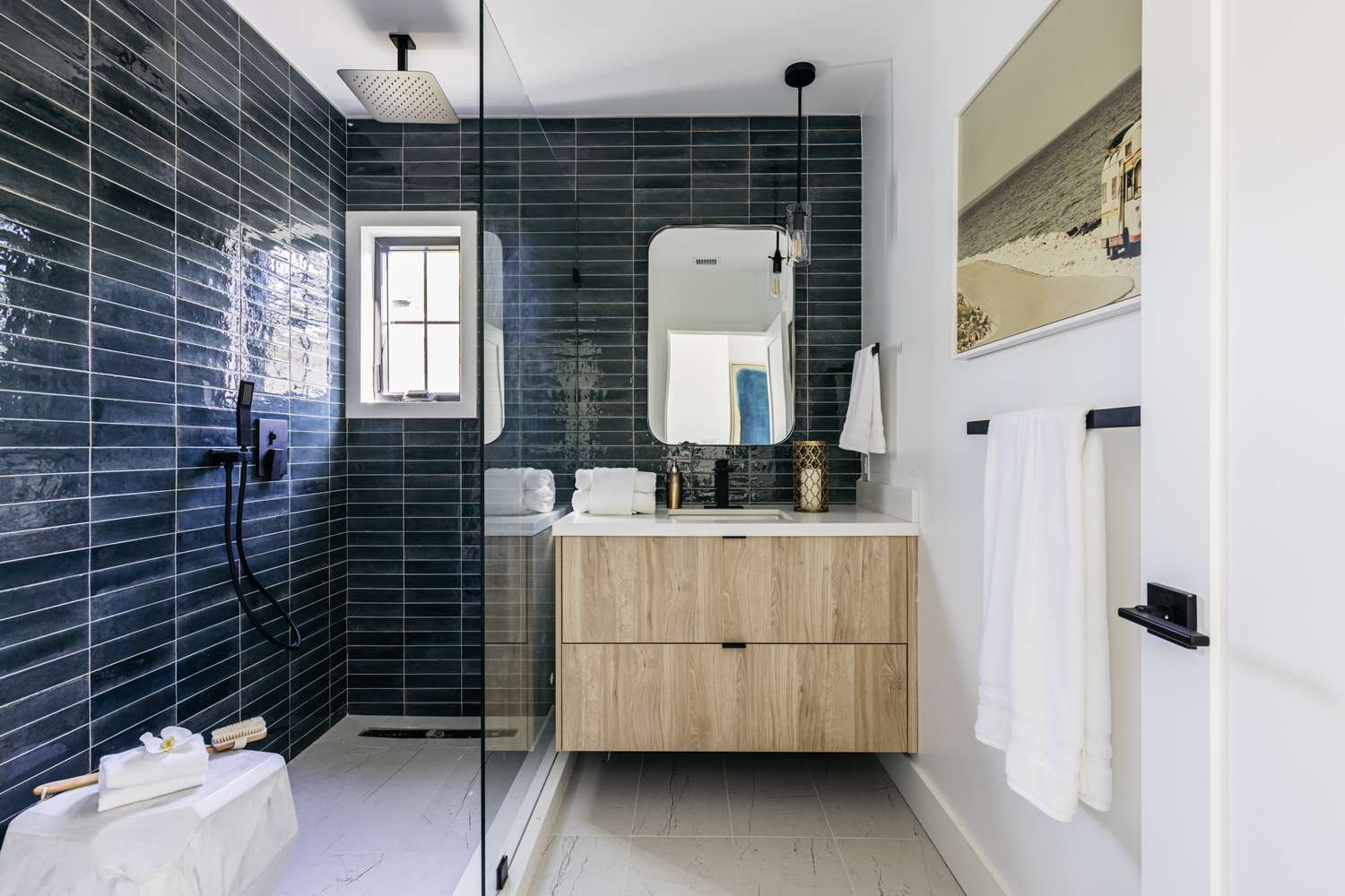 Puerta de mampara de baño de cristal junto a tocador revestido de madera y blanco en baño alicatado en azul oscuro