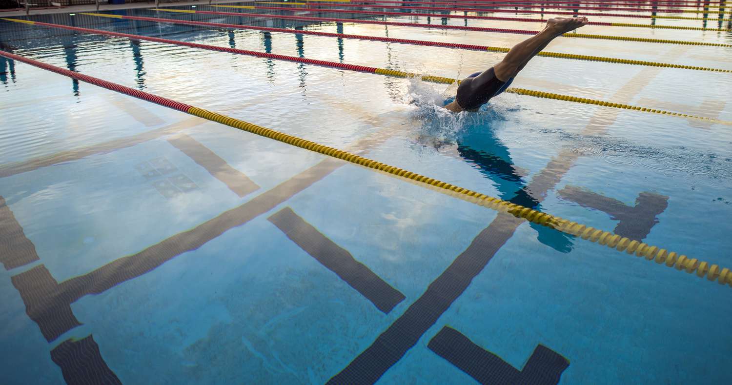 Pessoa mergulhando em uma piscina olímpica com divisores de pista.