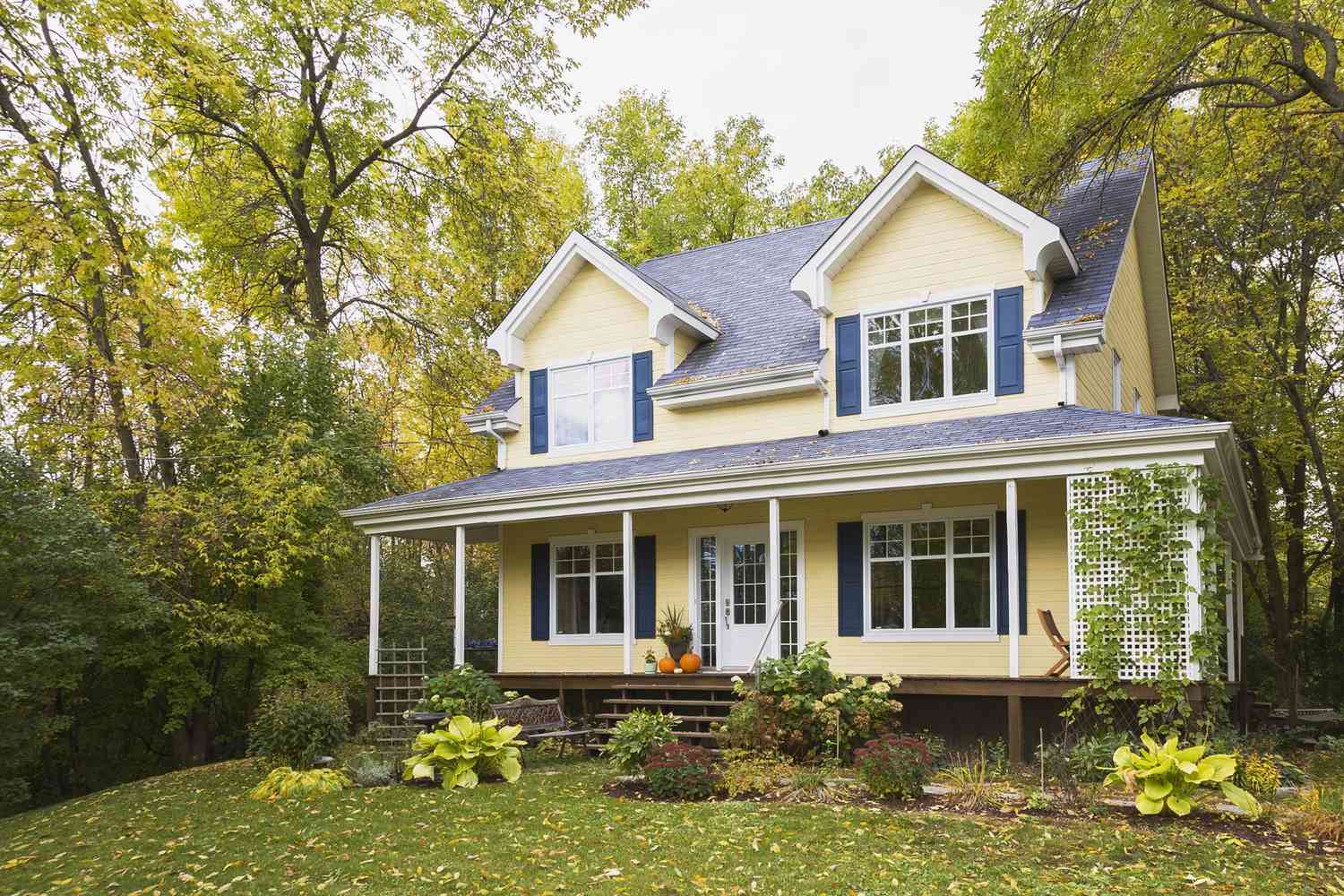 Fachada de casa de estilo cottage con tablas amarillas y adornos azules y blancos en otoño