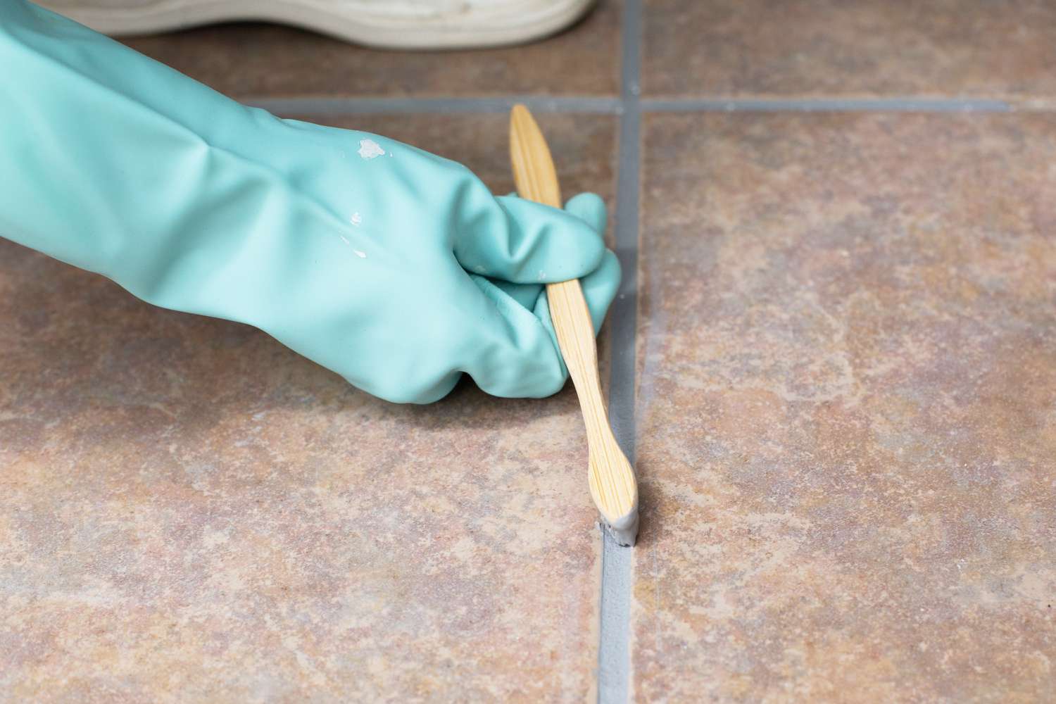 Gray grout colorant on old toothbrush added to grout between brown tiles with green glove