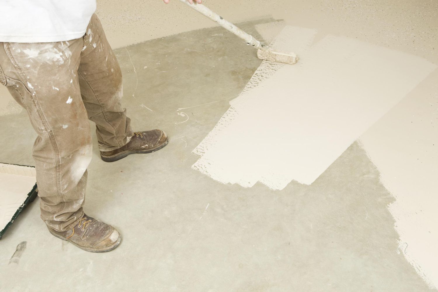 Painter rolling epoxy paint on concrete floor