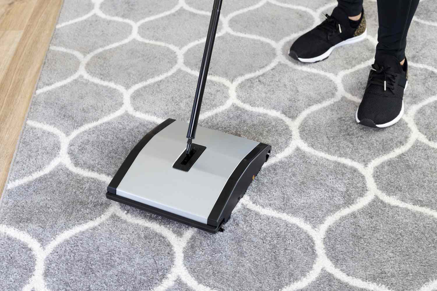Person using a carpet sweeper to clean a rug