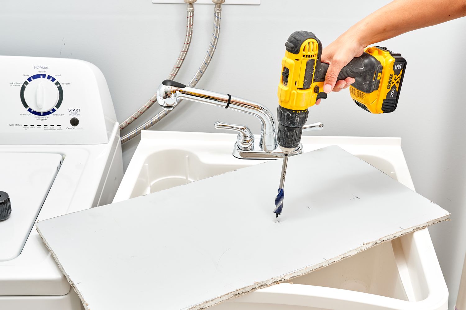 Square piece of cardboard on top of utility sink with electric drill creating hole