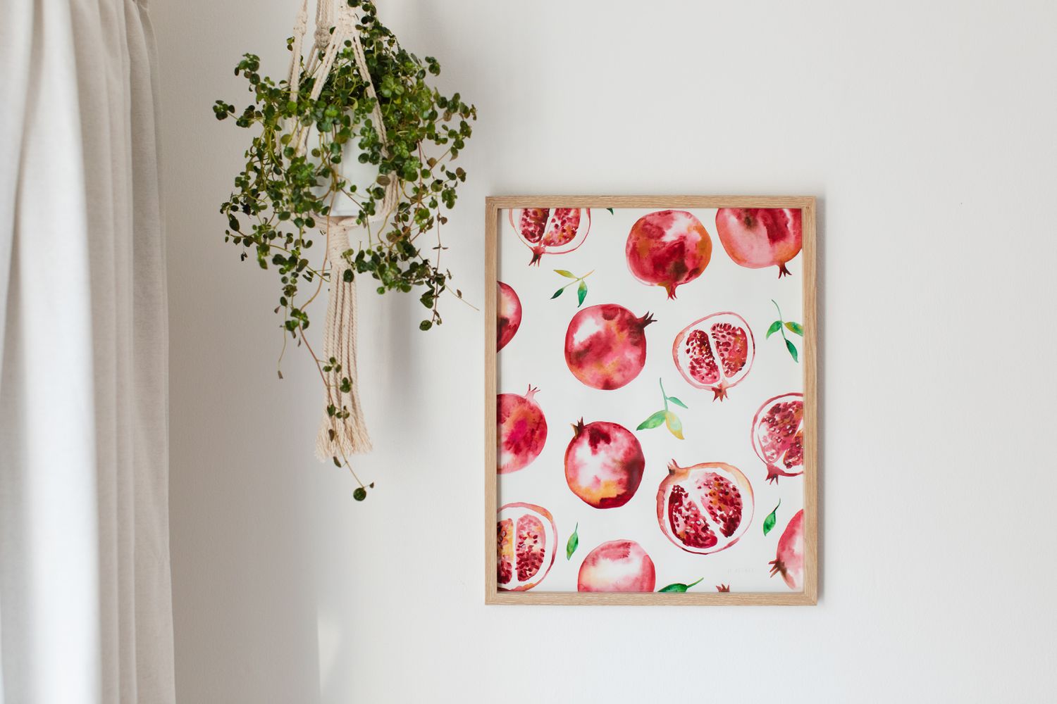 Framed art print of pomegranates on wall next to hanging houseplant