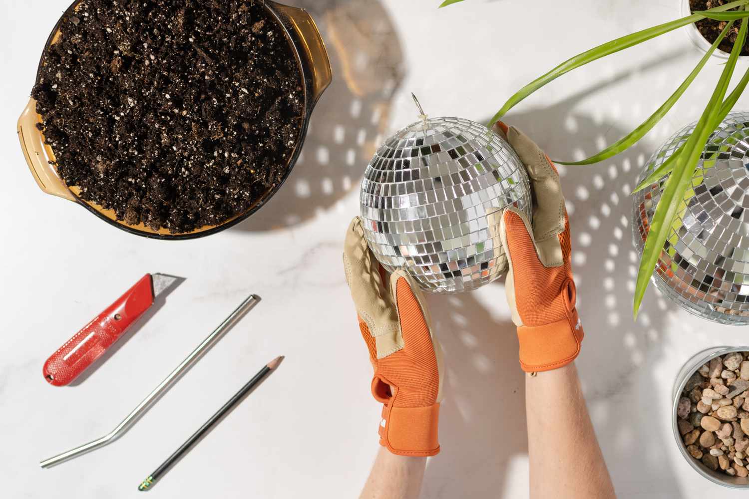 Orangefarbene Schutzhandschuhe, die die Discokugel neben den Materialien halten