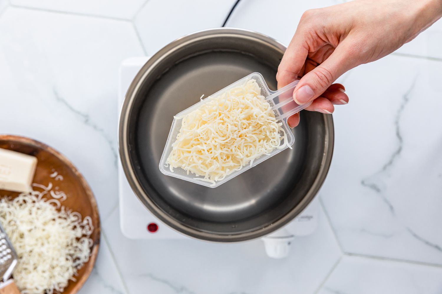 Détergent liquide DIY avec du savon râpé dans une cuillère en plastique au-dessus d'une casserole