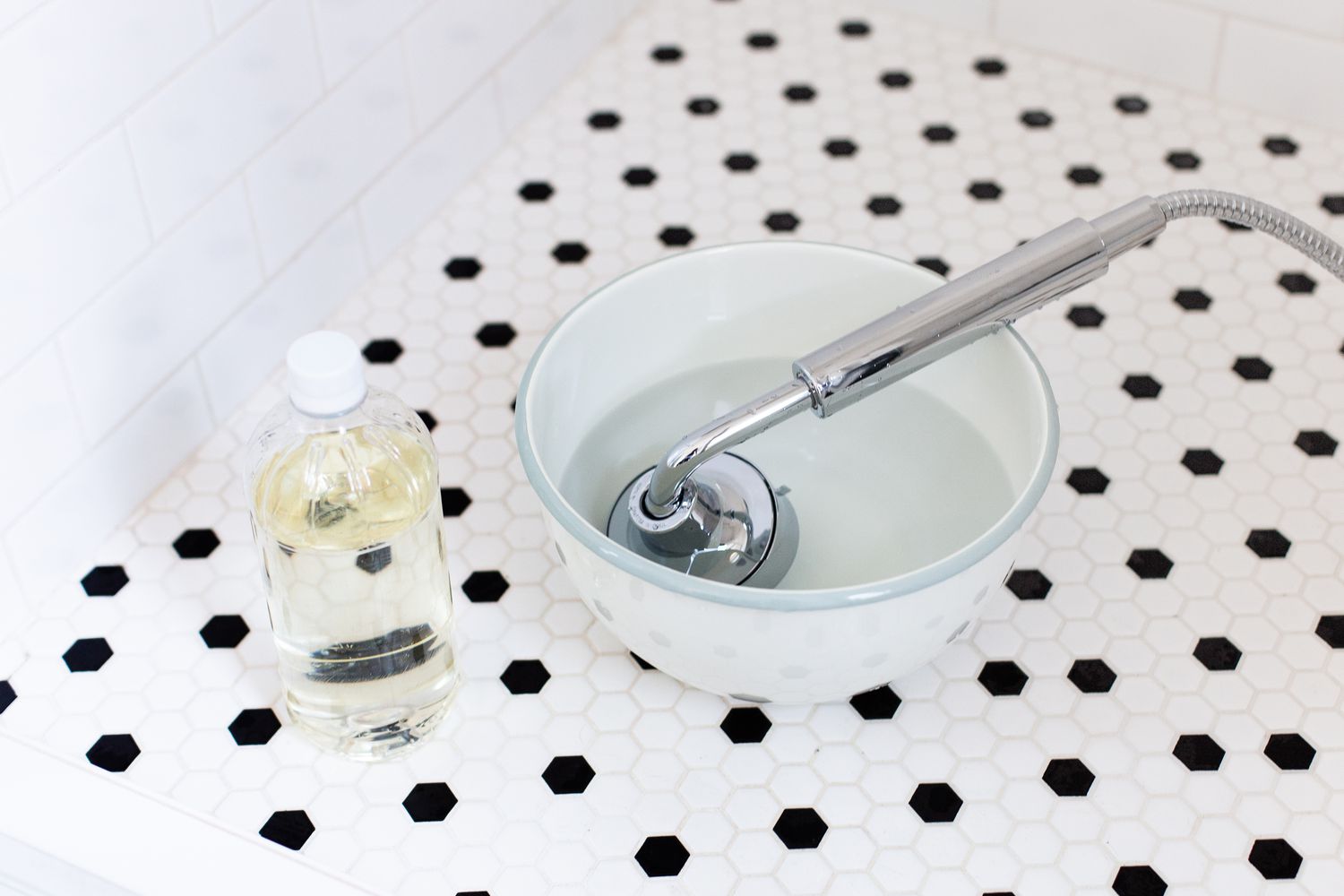 Showerhead submerged in bowl of white vinegar next to vinegar bottle