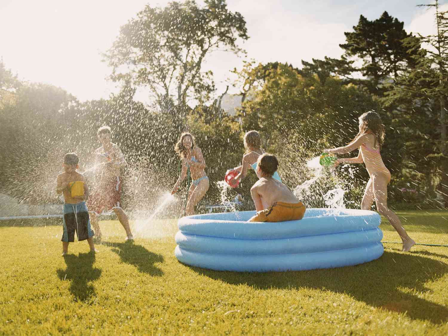 Uma piscina infantil azul na grama com crianças fazendo uma guerra de água.