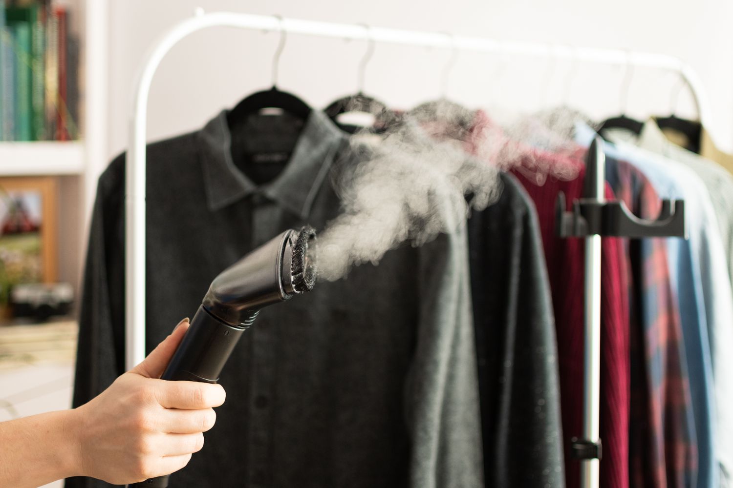 Clothes steamer with steam releasing in front of rack of clothes