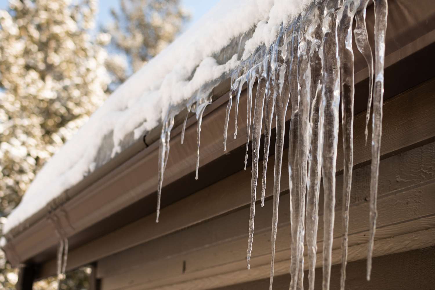 Hausdachrinne mit hängenden Eiszapfen und Schnee bedeckt