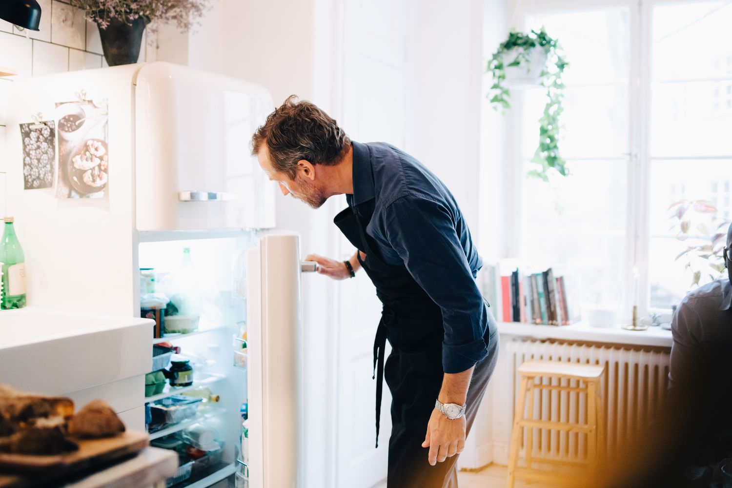 Man looking into refrigerator while standing at kitchen.