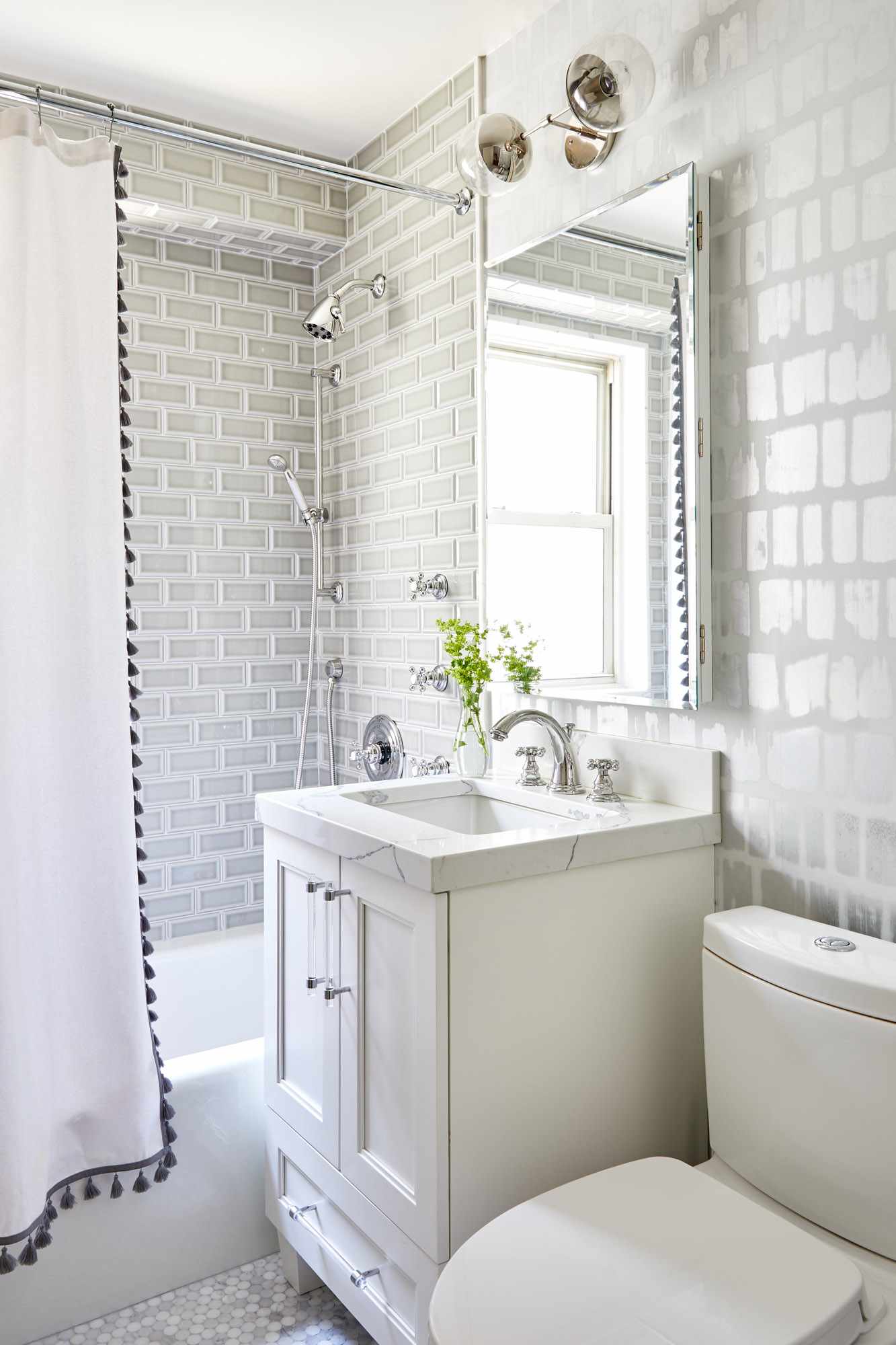 Baño con azulejo y papel pintado gris y cortina de ducha blanca con borlas negras