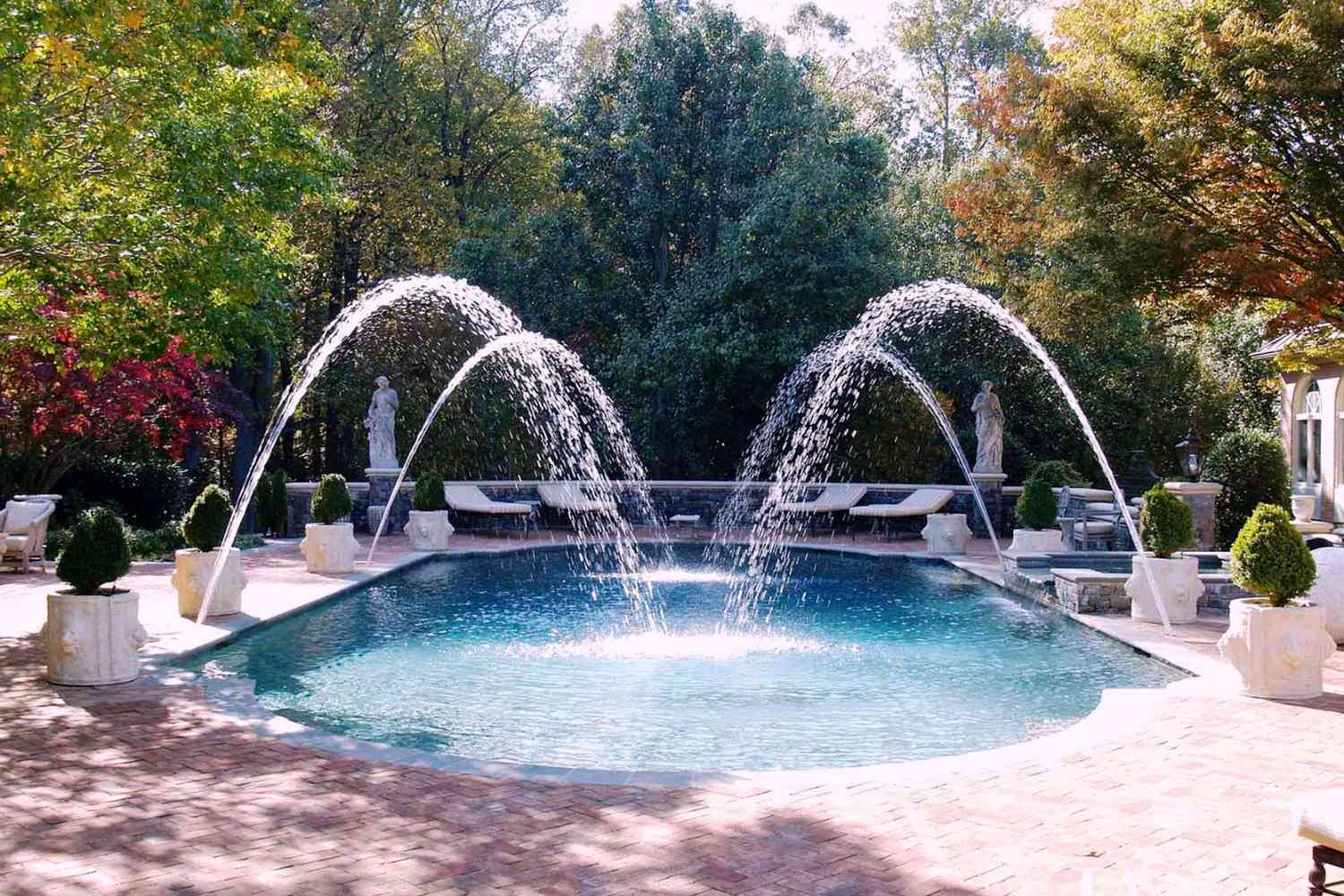 Mediterraner Pool mit Springbrunnen und Sträuchern in Töpfen.