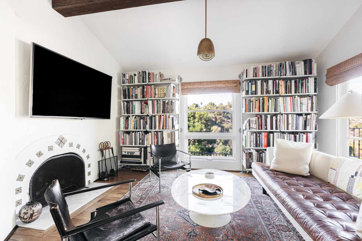 Large tv mounted on wall above small fireplace in living room with open book shelves