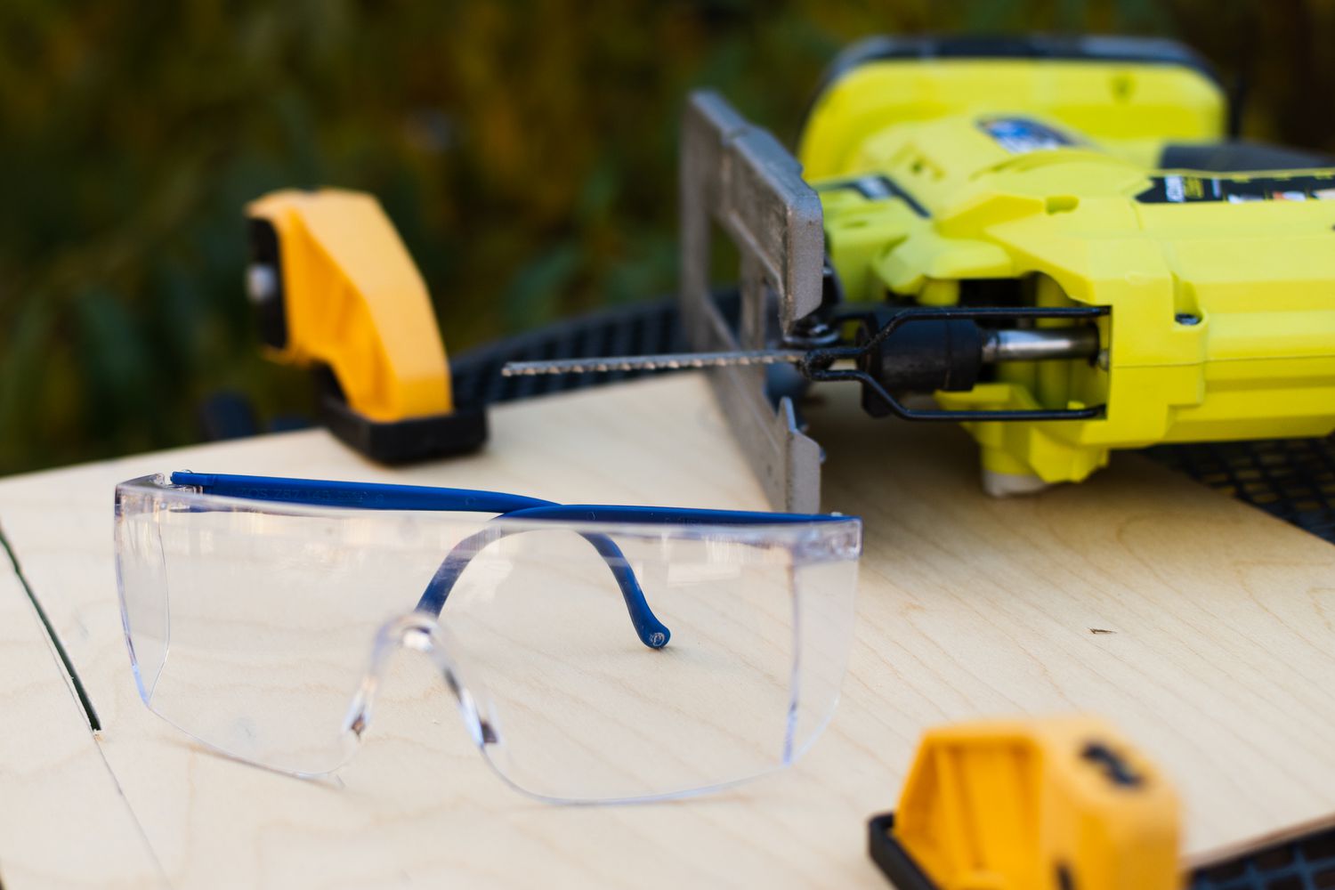 Óculos de segurança ao lado de uma serra tico-tico amarela em uma superfície de madeira em close-up