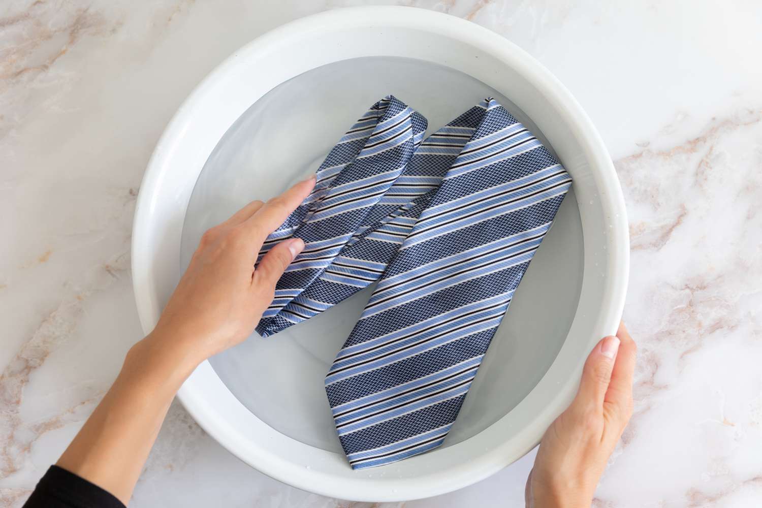 Cravate rayée bleue lavée à la main dans un bol blanc avec de l'eau et un prétraitement