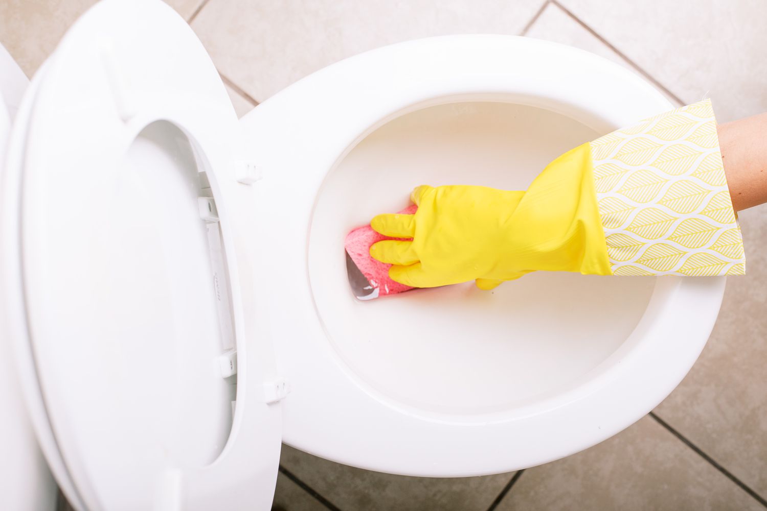 Rosa Schwamm, der mit gelben Handschuhen das Wasser aus der weißen Keramik-Toilettenschüssel aufsaugt