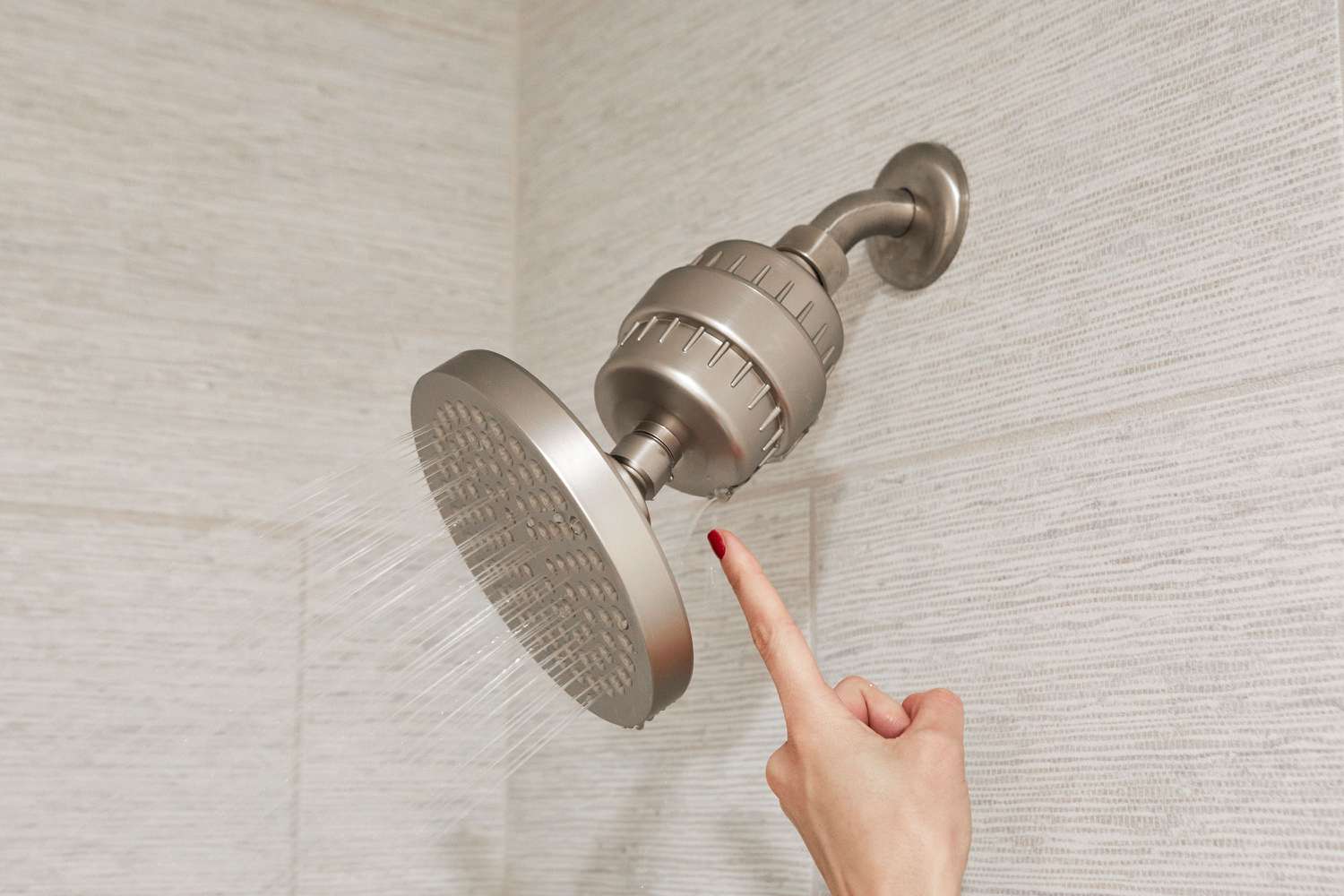 Finger pointing to leak from in-line shower filter on running shower head