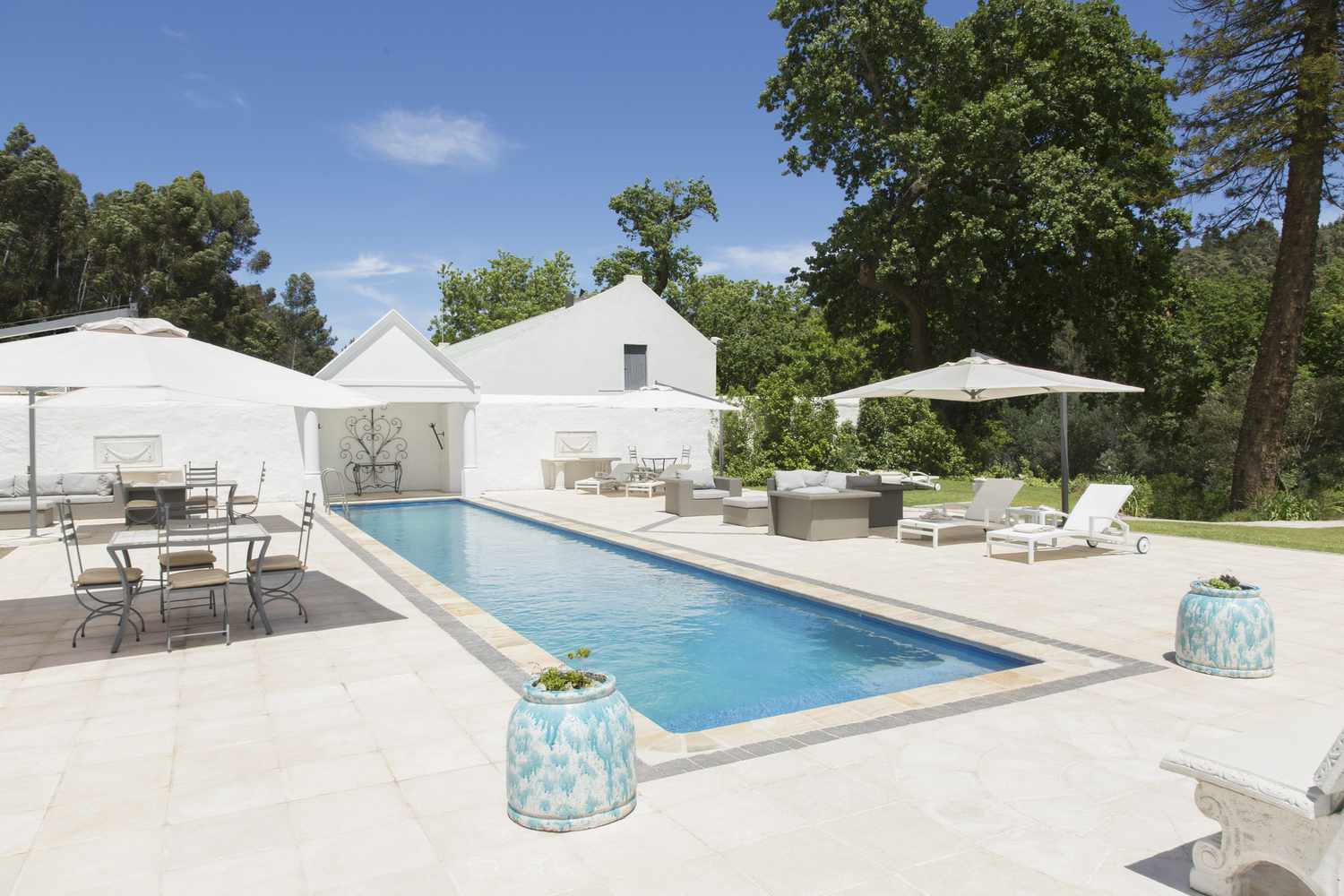 Uma piscina com azulejos brancos, móveis de pátio e guarda-sóis brancos.